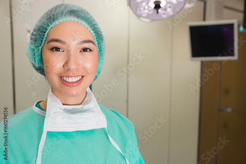 Asian woman surgeon standing in OR wearing surgical scrubs and cap under surgical light, copy space