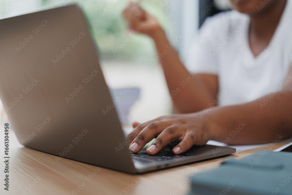 Naklejka premium Close-up of a student's hand typing on a laptop keyboard, celebrating the achievement of completing an online assignment or project from the comfort of home, radiating joy and excitement