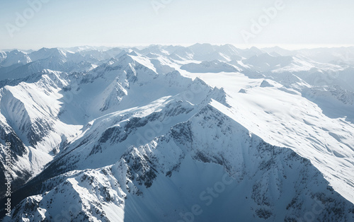 Aerial view of snow covered mountain range under a bright sky.