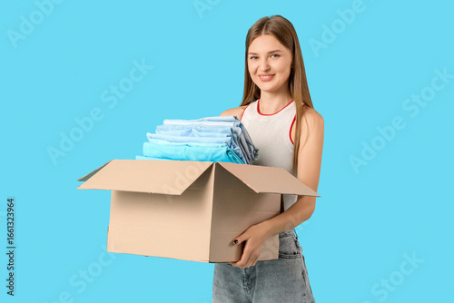Young woman holding box with clothes on blue background