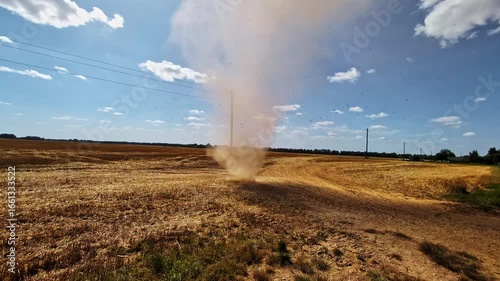 A sudden dust devil, small tornado, or whirlwind sand storm blows sand and debris into the sky above a field of freshly harvested crops during a drought