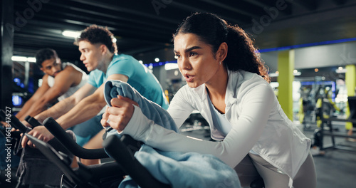 Fitness, spin class and people in gym on bicycle for cardio exercise, workout and training. Sports machine, health club and woman on stationary bike for cycling, endurance and challenge for wellness