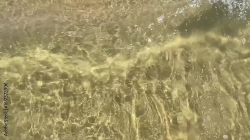Gekräuselte Wasseroberfläche am Strand mit Lichtreflexen und leichten Wellen, von oben , Zeitlupe