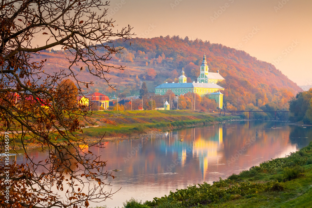 Fototapeta premium mukachevo, ukraine - 06 nov, 2015: urban landscape with river and trees in autumn. reflection of a monastery in the distance. beautiful travel destination of transcarpathia
