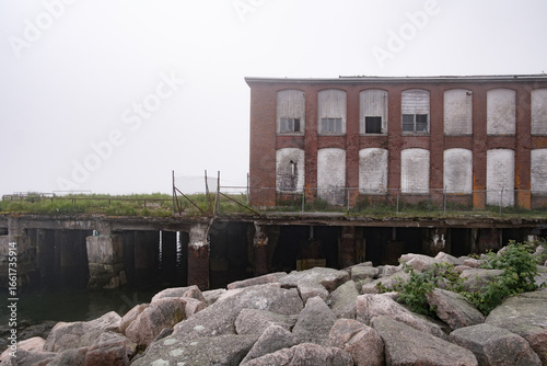 Abandoned brick building on a crumbling pier on a foggy day.