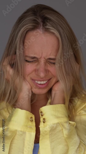 Vertical video of a young blonde woman covering her ears with her fingers and shaking her head, refusing to listen. Emotional denial, rejection, inner protest, sensory overload