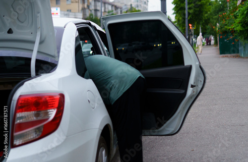 Person searching in the trunk of a parked car in an urban area during the early evening
