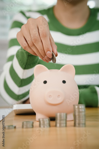 A person calculates finances while saving money, placing coins into a piggy bank. The scene symbolizes budgeting, investment, financial planning, and building future wealth with responsibility and dis