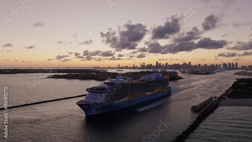 Aerial establishing view of a luxury cruise ship leaving Port of Miami at sunset. Cinematic Miami skyline, tropical waterfront, and small boats passing nearby with sunset light reflecting on ocean