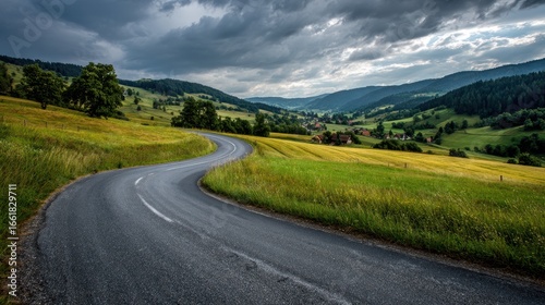 A long road with a curve and a hill in the background. The road is empty and the sky is cloudy
