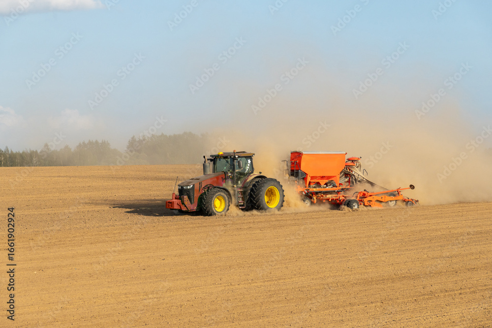 Obraz premium A tractor towing a seeder creates dust clouds while performing field work