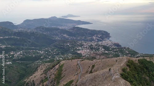 Mount Faito road seen from above, winding through the mountains with a spectacular view of the Sorrento Coast and Capri island in the distance. A scenic aerial perspective of Campania, Italy.