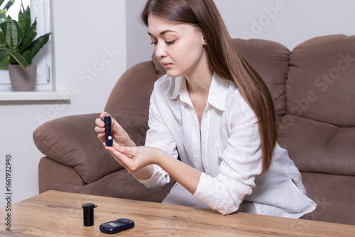 Photos Woman sitting on sofa and checking blood sugar with lancet device