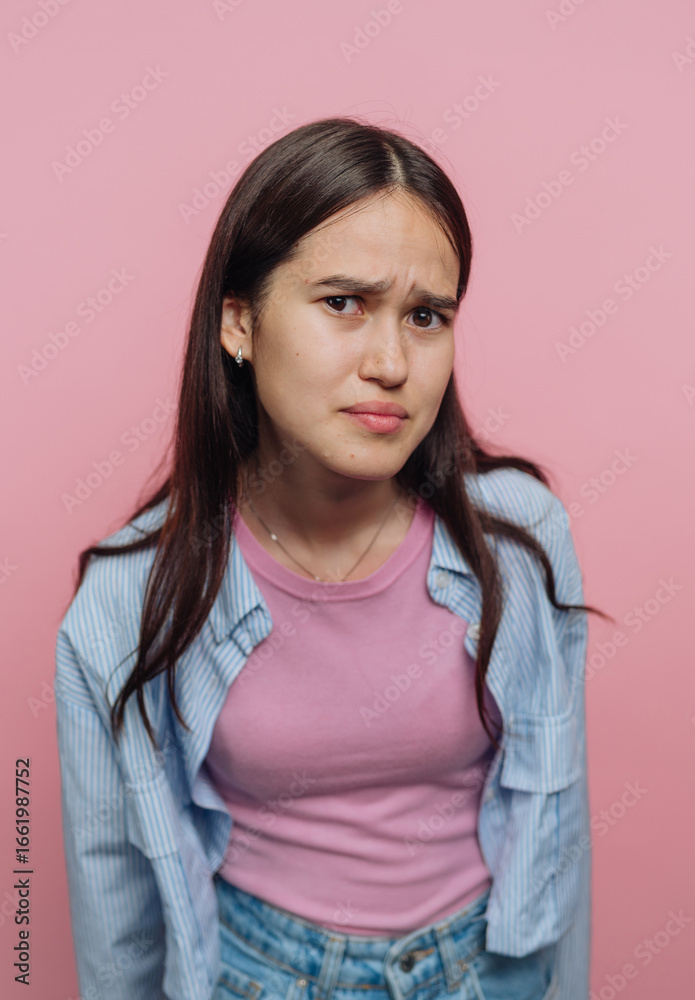 Fototapeta premium Young woman with a puzzled expression against a pink background.