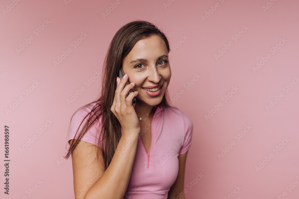 Fototapeta premium Smiling woman talking on a smartphone against a pink background.