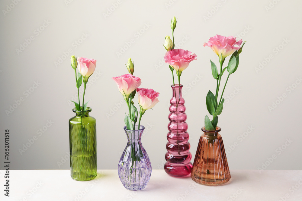 Beautiful eustoma flowers in glass vases on white table against light grey background Beautiful eustoma flowers in glass vases on white table against light grey background
