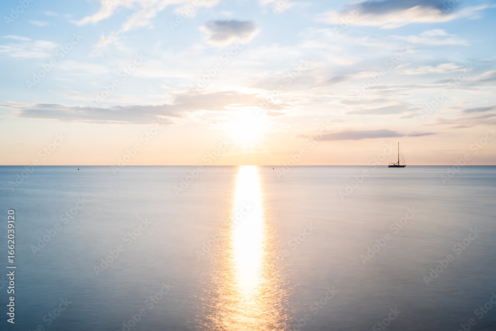 Obraz premium Langzeitbelichtung bei Sonnenuntergang am Meer mit Boot am Horizont