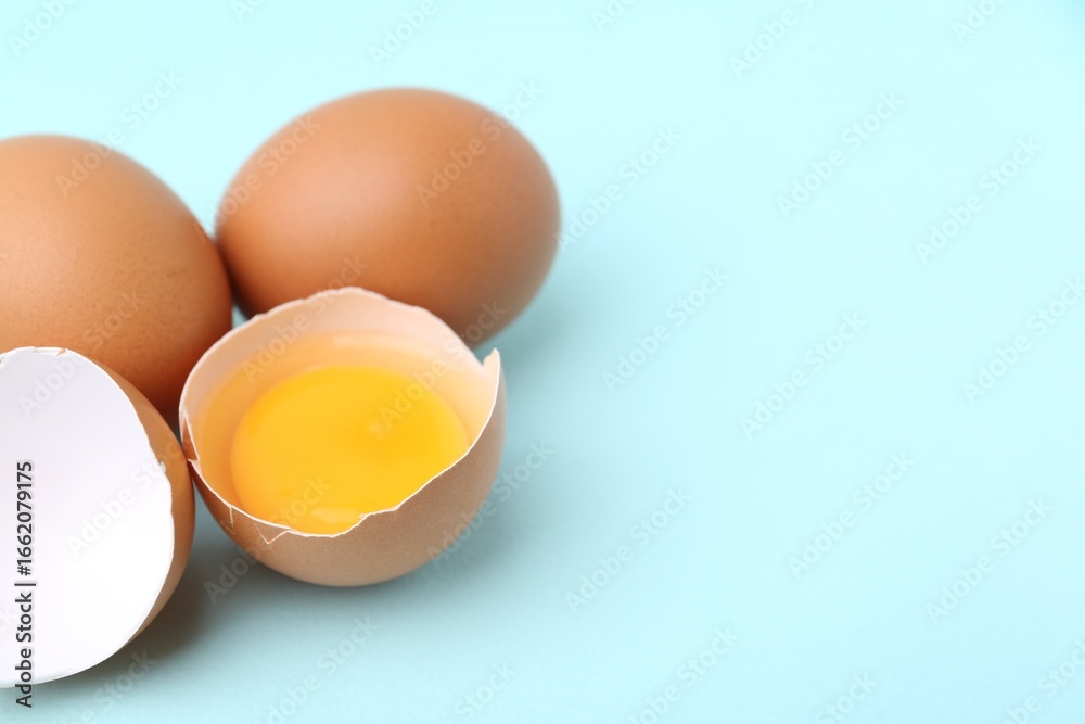 Whole and broken chicken eggs on light blue background, closeup. Space for text Whole and broken chicken eggs on light blue background, closeup. Space for text