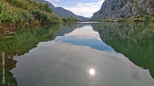 Morning calm on Cetina River canyon with mirror reflections of mountains, sky and sun