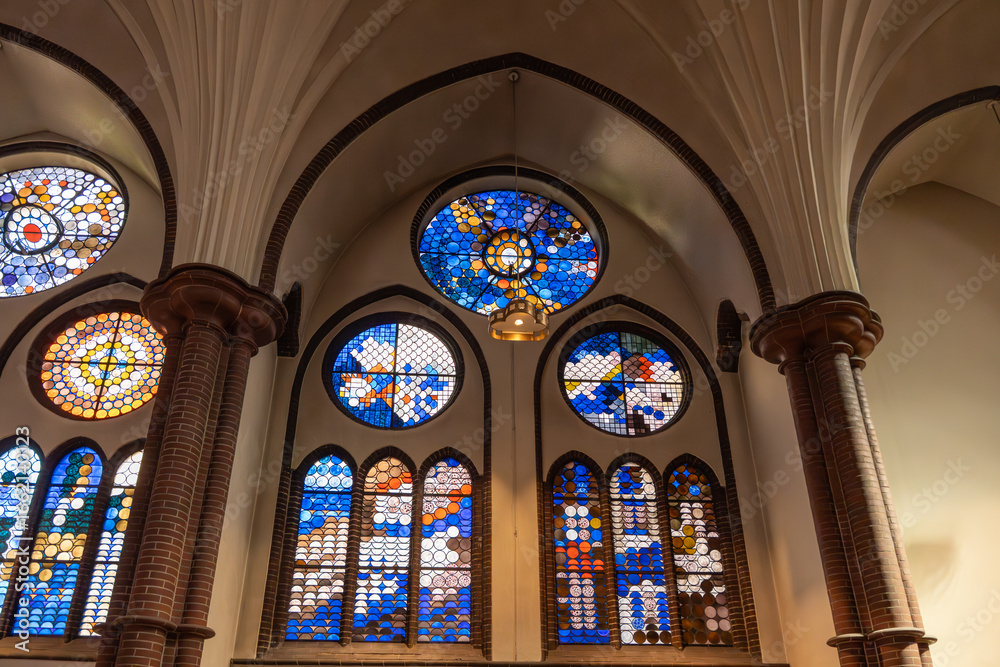 Fototapeta premium Colorful stained glass windows with abstract patterns allow colored light to enter the church. Gothic arches frame the windows.
