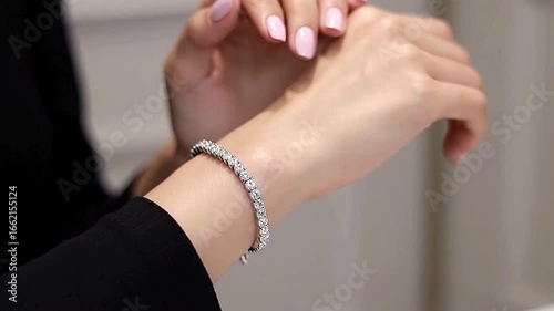 Womans arm with pink nails and a diamond bracelet against a blurred background