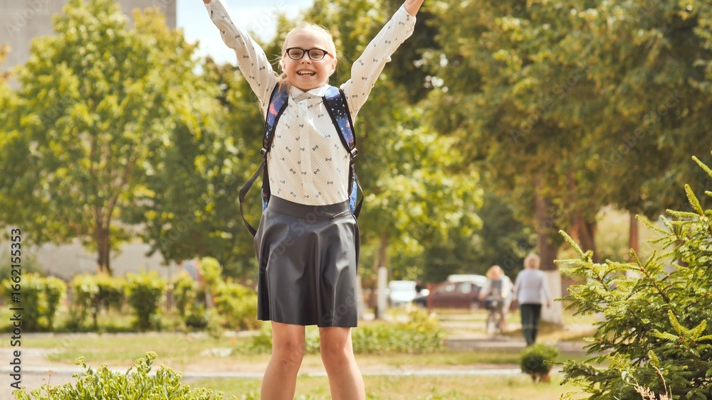 Obraz premium Excited schoolgirl jumping with arms raised in celebration after school, enjoying freedom and happiness in a park
