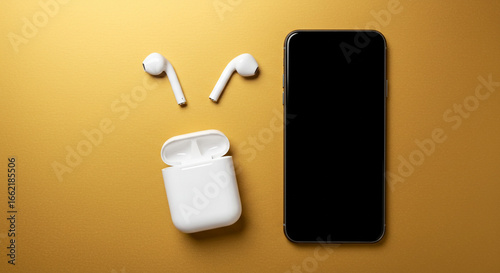 A top down shot of a smartphone with a black screen and white earbuds on a golden yellow background