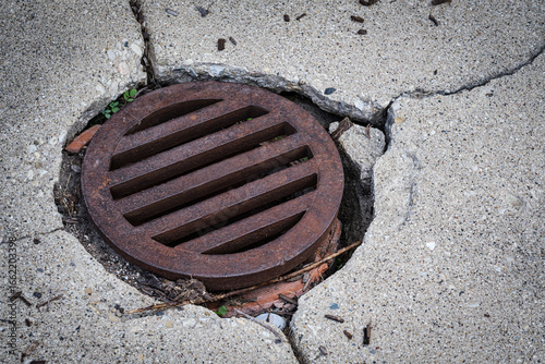 rusty metal sewer grate with crumbling concrete infrastructure