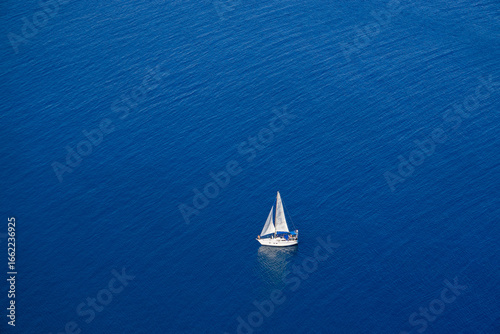 Yacht with white sails on a blue sea background. Top view.