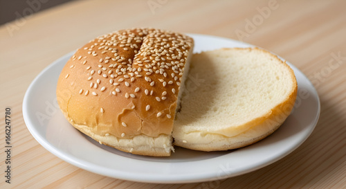 A burger bun with sesame seeds, plain, no fillings, on a plate.