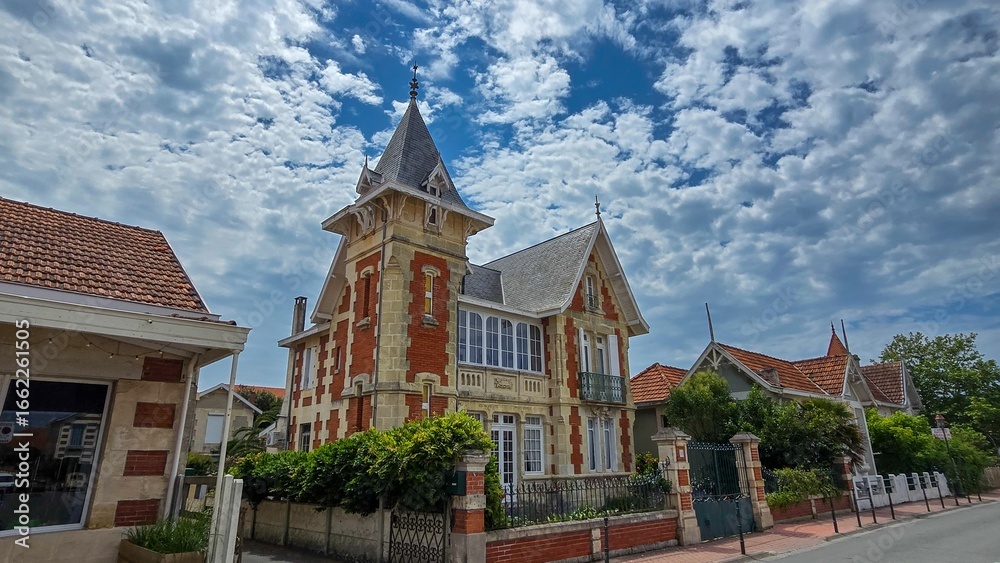 Naklejka premium One of charmante villas in the picturesque resort town Soulac-sur-Mer on the Atlantic, France. Against the background of a blue sky with white clouds.