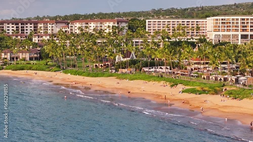 Aerial view of beautiful ocean sea waves on coastline with upscale villa condo resorts and vacation homes in Wailea Maui, Hawaii during sunset with people beach on oceanfront landscape - 4K Drone