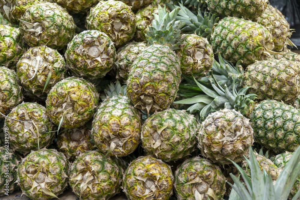 Fototapeta premium Fresh pineapples stacked in bulk at a market stall.