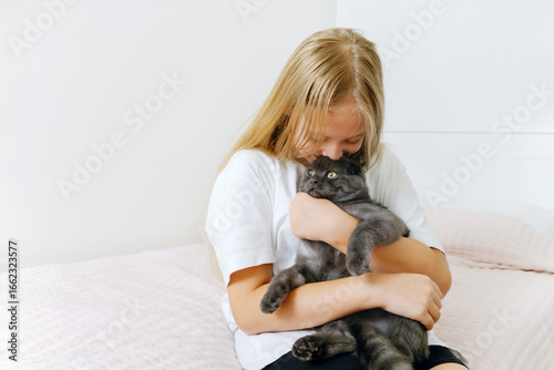 Obraz na plátně Girl in a light room holding and hugging a gray cat