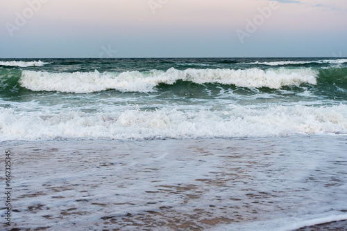 Strong ocean waves breaking on sandy beach at sunset