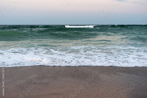 Ocean waves rolling onto sandy beach with foam at sunset