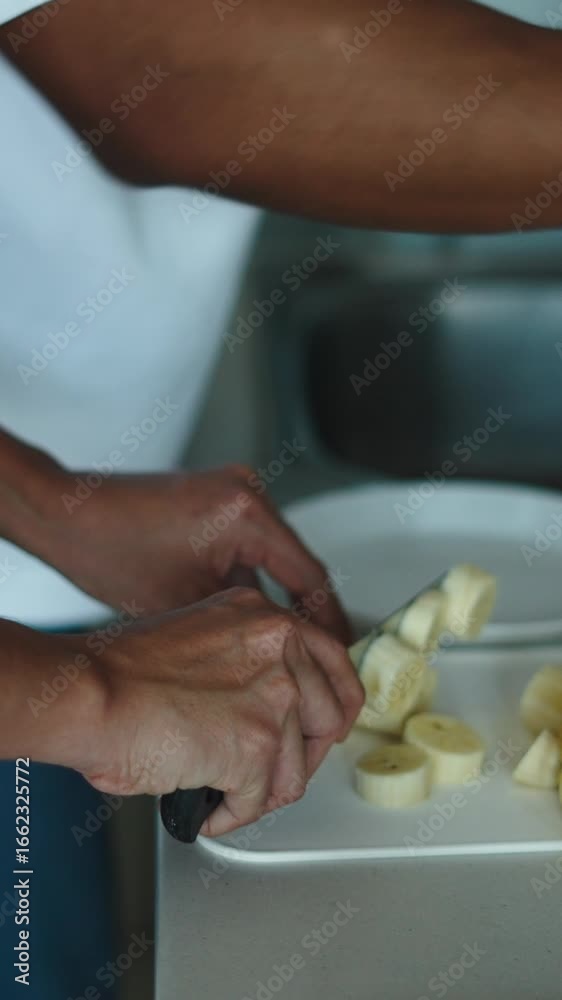 Interracial couple preparing food, slicing banana on white cutting board Interracial couple preparing food, slicing banana on white cutting board