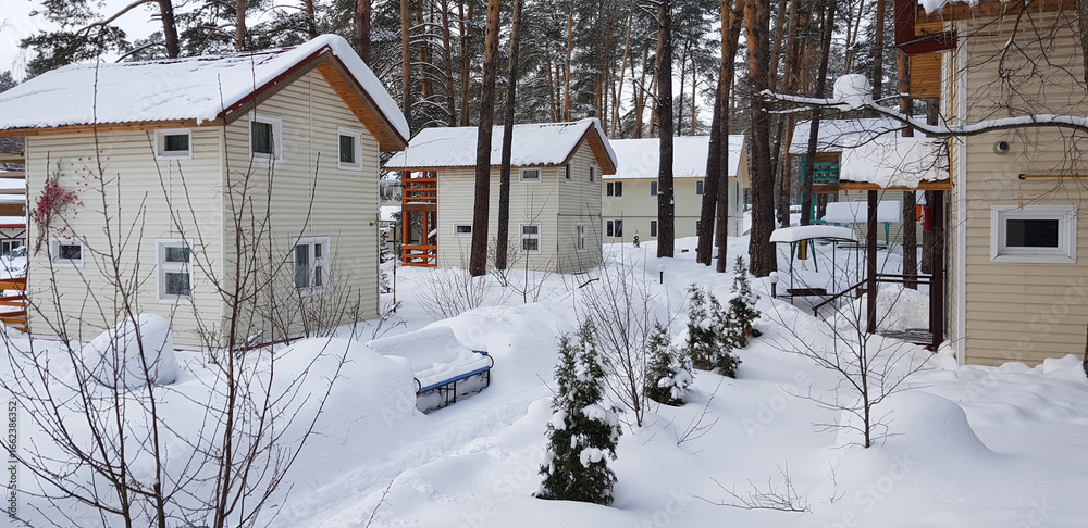 a winter village with neat two-story light-colored houses located among tall pine trees. a winter village with neat two-story light-colored houses located among tall pine trees.