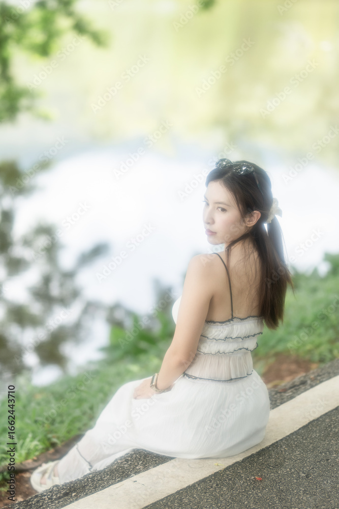 Naklejka premium Woman in a long light dress is resting by the lake enjoying the view.