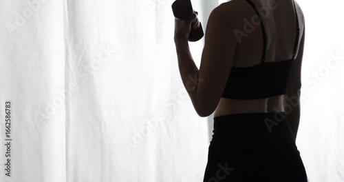 Woman from the back, lifting dumbbells, symbolizing fitness and a commitment to a healthy lifestyle for overall wellness, a healthy and fit lifestyle. Good habits for a balanced life