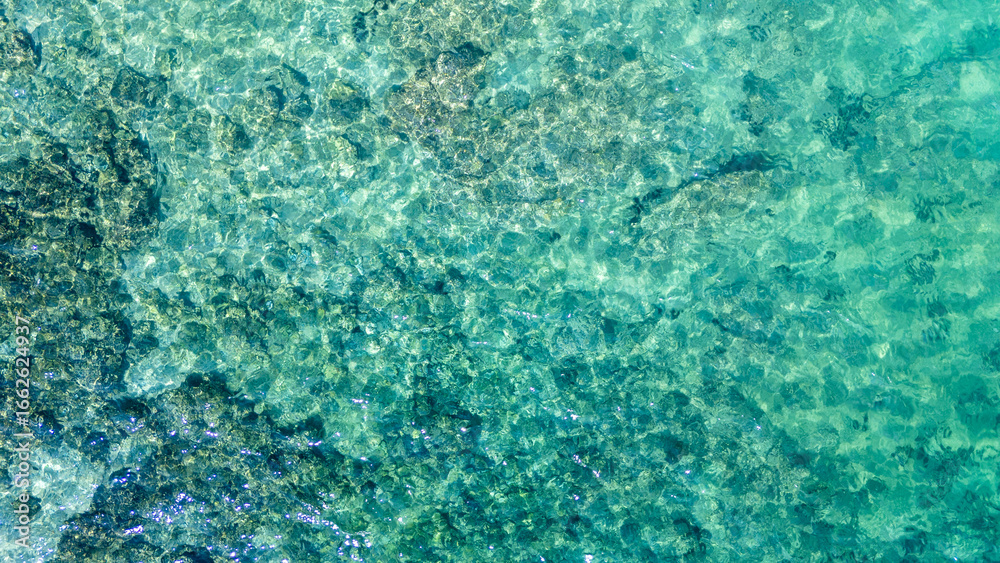 Fototapeta premium Aerial top view of crystal-clear turquoise sea water with visible underwater texture. Ideal for backgrounds, travel promotions, and marine environment concepts.