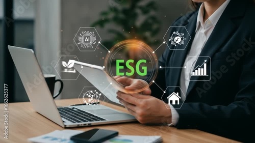 Woman in suit using tablet with esg graphic overlay on desk with laptop and coffee mug nearby view