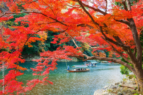 Boatman punt wooden tourist boat along Arashiyama river in autumn