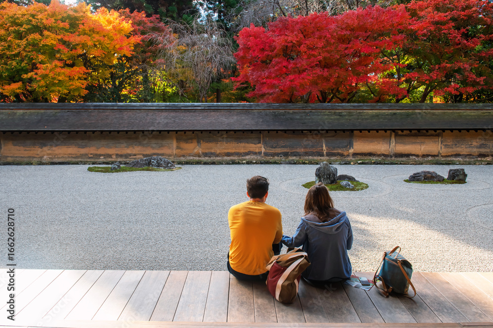 Fototapeta premium Foreign couple sit enjoy rock garden in fall at Ryoan-ji temple, Kyoto
