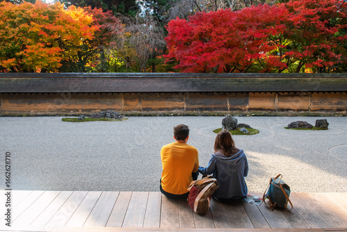 Foreign couple sit enjoy rock garden in fall at Ryoan-ji temple, Kyoto