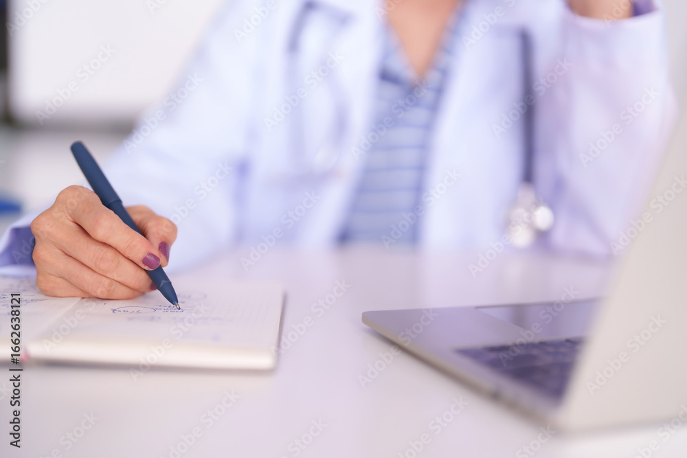 Fototapeta premium Adult Asian doctor hand writing notes in notebook at medical office desk healthcare professional working diligently on research studies