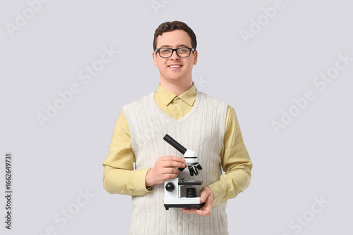 Young male teacher with microscope on grey background