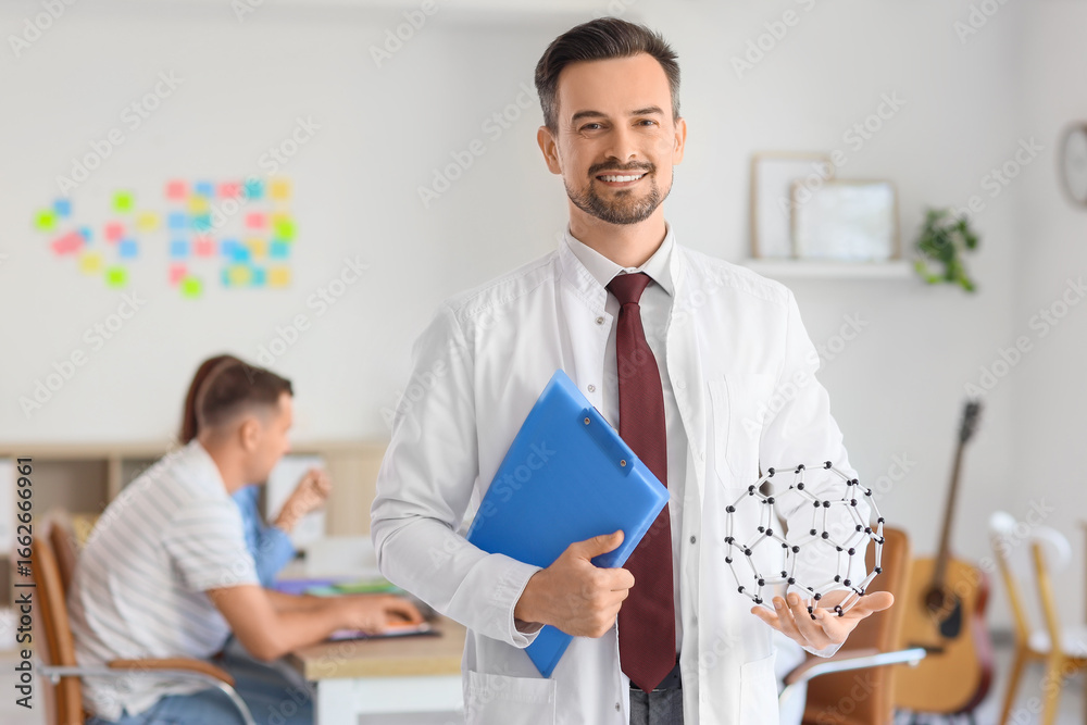 Fototapeta premium Male Science teacher with clipboard and molecular model in school office