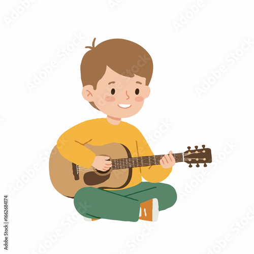 A young boy with brown hair sits cross-legged, smiling, while playing an acoustic guitar.