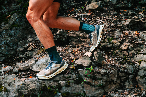 Worn trail running shoes on rocky terrain with a professional runner on rugged natural ground, close-up on muscular legs